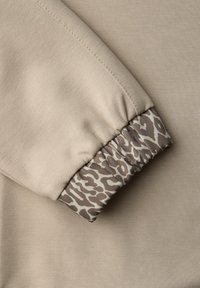 Beige sweatshirt med en tekstureret overflade og elastiske manchetter med leopardmønster i nuancer af brun og creme.