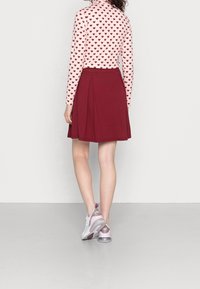 Lichtroze top met lange mouwen en kleine donkere hartjes, gecombineerd met een knie-lange bordeauxrode geplooide rok en lichtpaarse sportschoenen.