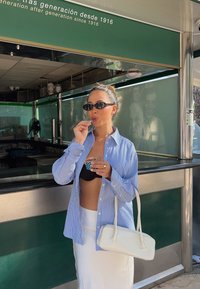 Striped blue and white button-up shirt, black bikini top, white skirt, holding a small ice cream cup, accompanied by a white handbag.