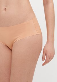 Laiškaina krēmkrāsas bezšuvju bikini biksītes ar vidēju jostas augstumu, gludu tekstūru un reljefa zīmola nosaukumu jostā.
