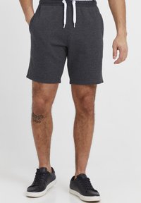 Shorts gris en tissu doux, dotés d'une taille avec cordon de serrage, de poches latérales et d'une coupe décontractée. Portés avec des baskets noires.