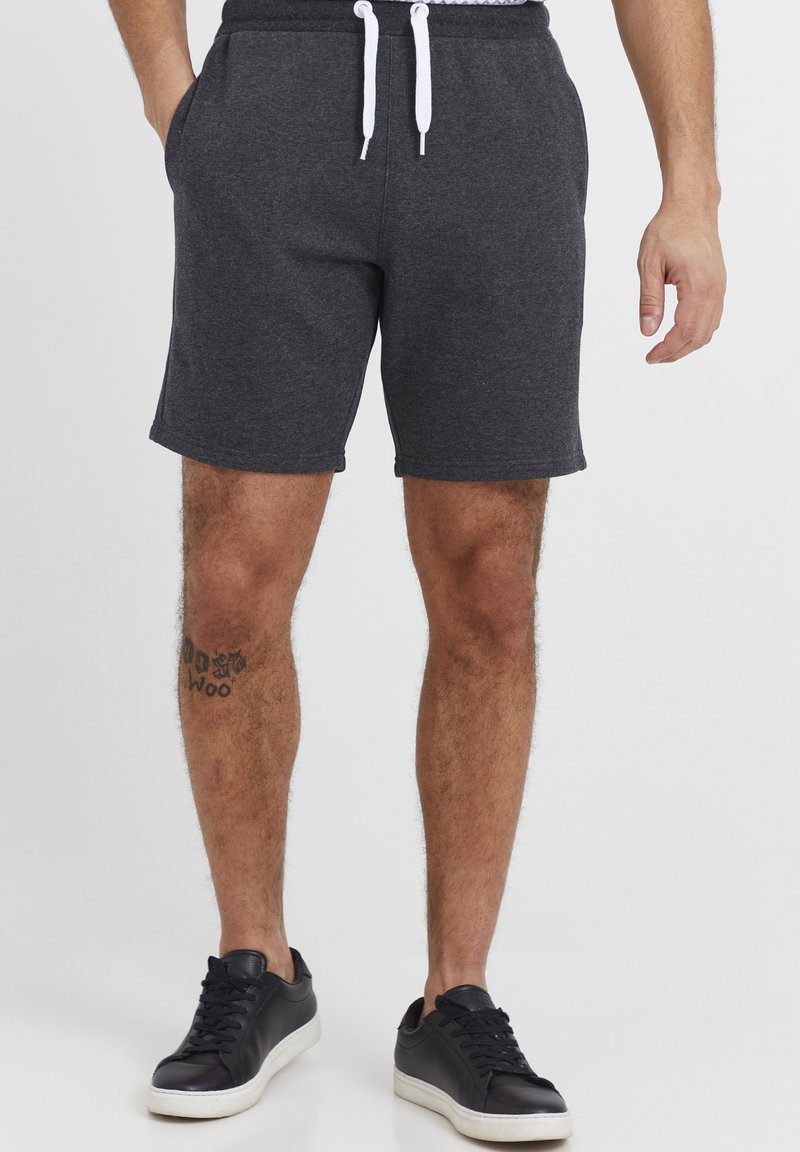 Shorts gris en tissu doux, dotés d'une taille avec cordon de serrage, de poches latérales et d'une coupe décontractée. Portés avec des baskets noires.