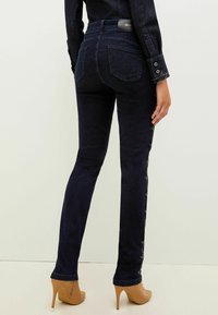 Tummansiniset farkut, joissa on istuva leikkaus ja koristeommeltu sauma sivuilla. Yhdistetty vaaleanruskeisiin korkokenkiin.