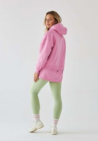 Różowa, oversize'owa bluza z kapturem, zielone legginsy, białe sneakersy z różowymi akcentami. Miękka tkanina, luźny krój, długie rękawy i kieszeń typu kangurka.