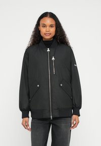 Μαύρο bomber μπουφάν με φερμουάρ μπροστά, δύο πλαϊνές τσέπες, ριμπ μανσέτες και ομοιόμορφη υφή. Διαθέτει λεπτομέρεια τσέπης με φερμουάρ στο στήθος.