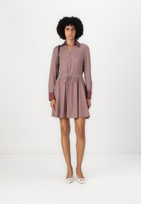 Rochie cămașă cu buline roșii și albe, cu mâneci lungi, talie strânsă și fustă în formă de A. Prezintă un gât tip cămașă și mansete contrastante.