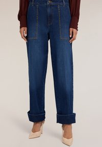 Vaqueros de mezclilla en azul oscuro con un corte holgado, con bolsillos remachados y puños enrollados. Se complementan con zapatos de tacón alto nude.