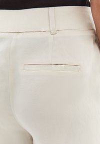 Pantaloni beige su misura con una texture liscia, dotati di una singola tasca posteriore e dettagli di cucitura discreti in vita e all'apertura della tasca.