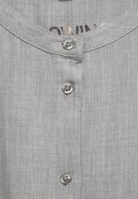 Camicia di lino grigia chiara con scollatura rotonda, caratterizzata da chiusura a bottoni sulla parte anteriore e un tessuto leggermente strutturato.