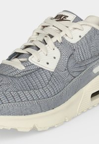 Γκρι και λευκό αθλητικό παπούτσι Nike με υφή που μοιάζει με δέρμα ερπετού, λευκά κορδόνια και ορατό αερόσακο στη σόλα.