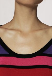 Červený, růžový a fialový pruhovaný tílko s širokým černým výstřihem. Vyrobeno z hladké látky s přiléhavým střihem.