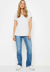 Top bianco a maniche corte con scollo a V e dettagli con bottoni, abbinato a jeans in denim azzurro chiaro a gamba dritta e sneakers bianche.