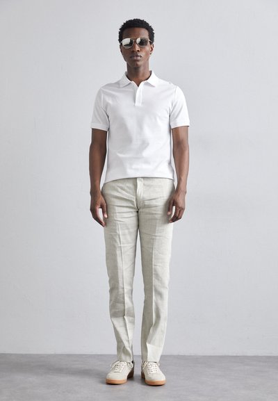 Valge lühikeste varrukatega polo särk, beežist linast pükstest ja beežist spordijalanõudest koosnev komplekt. Aksessuaaridena tumedad päikeseprillid. Minimalistlik ja juhuslik outfit.