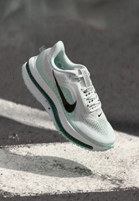 Baskets blanches avec le logo Nike noir, semelle vert menthe, tige en mesh texturé, design léger et accents à motifs.