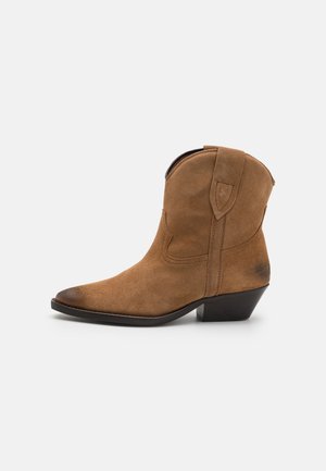 Bottine cowboy en daim marron à bout pointu, talon bas empilé et tirettes sur les côtés ; texture lisse et subtils détails de couture.