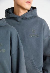 Süsinikhall kapuutsiga pluus, millel on mugav lõige, ees tasku ja tikitud "VERTERE BERLIN" logo rinnal. Puuvillane materjal.