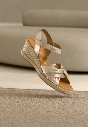 Sandale cu platformă, culoare bej, cu platformă împletită, bretea frontală cu nod și curea la gleznă, expuse pe o suprafață texturată neutră.