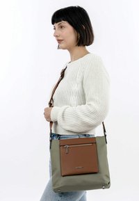 Lehká, obdélníková crossbody taška v olivově zelené barvě s přední kapsou z hnědé kůže, se zipovým uzavíráním a nastavitelným popruhem.