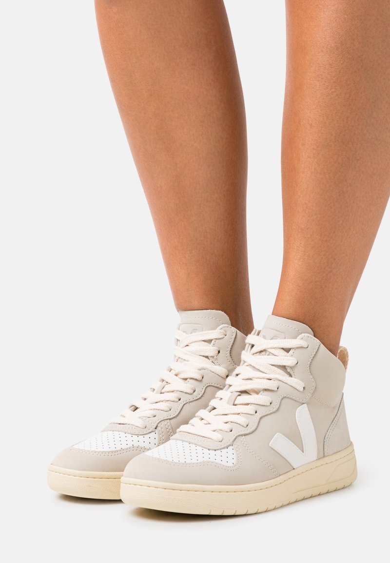 Hnědé vysoké sneakers vyrobené z kůže, s bílými akcenty, texturovanými perforacemi na špičce a krémovou gumovou podrážkou.