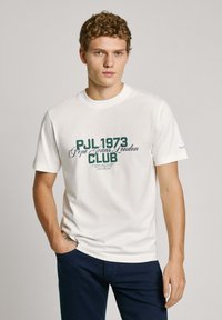 Balta medvilninė marškinėliai su apvaliu kaklu, su žaliu tekstu: "PJL 1973 Pepe Jeans London KLUBAS" per krūtinę. Laisvas sijonas, trumpomis rankovėmis.