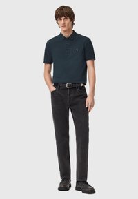 Dunkelblaues Polohemd mit Kragen und drei Knöpfen, kombiniert mit schwarzen geraden Jeans und schwarzen Schuhen. Einfaches Design, ohne Muster.