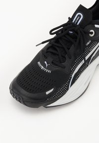 Scarpa da corsa nera con tomaia in mesh, superficie texturizzata e dettagli riflettenti. Presenta lacci, colletto imbottito e suola ammortizzata.