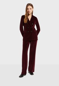Burgundské sametové sako s dvojitým zapínaním a čiernymi gombíkmi, doplnené o široké nohavice. Hladká textúra a priliehajúci strih.