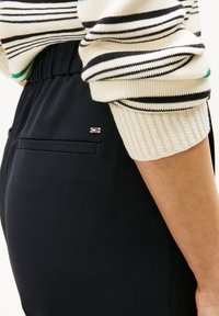 Granatowe spodnie wykonane z gładkiej tkaniny, z elastyczną talią, bocznymi kieszeniami oraz małym logo na tylnej kieszeni. Sweter w paski z dzianiny.