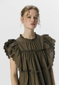Braunes Rüschkleid mit gewelltem Ärmel und gerafftem Oberteil. Hergestellt aus einem glatten Stoff mit einem subtilen Glanz.