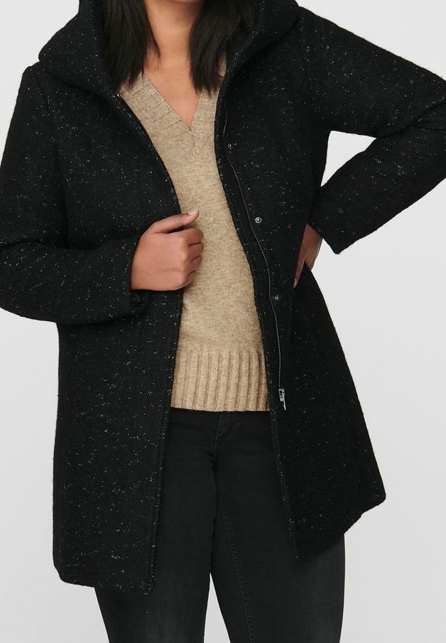 Abrigo negro con capucha en tejido texturizado, cierre con cremallera, que presenta un ajuste relajado y bolsillos. Lleva puesto un suéter de punto beige.