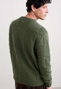 Maglione verde lavorato a maglia con un motivo testurizzato, dotato di scollo rotondo e orlo a coste. La parte posteriore mostra un design quadrato con tonalità varie.