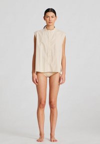 Beige, ärmlös skjorta med hög krage och knäppning fram, tillverkad av ett slätt tyg. Enkelt övergripande mönster.