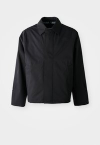 Veste noire courte avec col évasé, deux poches avant et manches longues. Fabriquée dans un matériau lisse et léger avec un branding subtil.