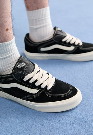 Sorte ruskinds sneakers med hvide accenter, fremtrædende snørebånd og gummisåler. Har logo-patch på tungen og kontrasterende syninger.