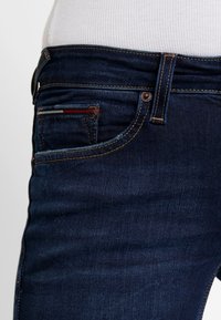 Mörkblå denimjeans med slim fit. Noterbara detaljer inkluderar kontrasterande sömmar, en liten bakficka och en färgad accentrand.