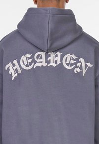 Hettegenser i dempet grå med hvit brodert tekst "HEAVEN" på baksiden. Glatt stoff med en avslappet passform og kengurulomme.