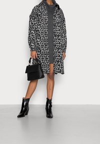 Cappotto leopardato in grigio e nero, abbinato a un vestito grigio. Borsa nera con manico e stivaletti neri con tacco. Texture lisce.