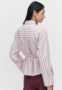 Striped shirt in light pink and white, featuring a peplum waist, long sleeves, and a collar. Smooth texture with button accents.