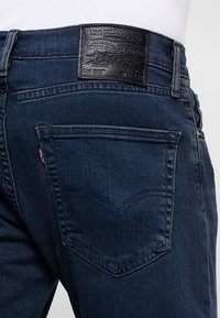 Mörkblå denimjeans med en läderlapp märkt "Levi Strauss & Co." på midjan, med bakfickor och kontrasterande sömmar.
