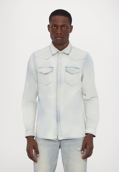 Light blue denim shirt with long sleeves, pointed collar, two chest pockets, and button closure. Features fading and subtle stitch detailing.