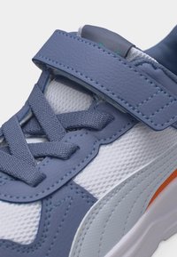 Κοντινό πλάνο ενός μπλε και λευκού αθλητικού παπουτσιού με υφασμάτινη υφή, μπλε κορδόνια, μπλε λουράκι και λευκή σόλα με πορτοκαλί λεπτομέρεια.