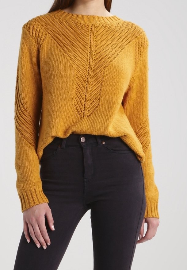 Senfgelber, gestrickter Pullover mit einem strukturierten Zickzackmuster auf der Vorderseite und gerippten Bündchen; kombiniert mit figurschmeichelnden schwarzen Jeans.