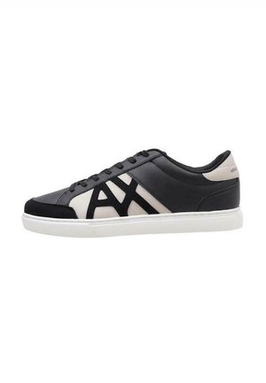 Zapatilla en blanco y negro con parte superior de cuero suave, diseño con cordones, acentos en negro que contrastan y suela de goma blanca.