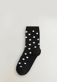 Czarna skarpetka w białe kropki, wykonana z elastycznego materiału, z wzmocnionym palcem i ściągaczem dla wygody i dopasowania.