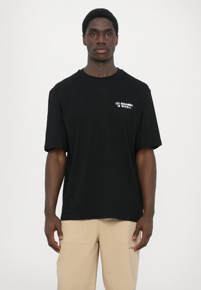T-shirt en coton noir avec manches courtes et col rond, arborant le texte blanc "LES BENJAMINS" sur le côté gauche et une coupe décontractée.