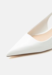 Λευκό γυναικείο παπούτσι ψηλοτάκουνο με μυτερή μύτη, λεία επιφάνεια και μπεζ εσωτερική επένδυση σε απλό φωτεινό φόντο.