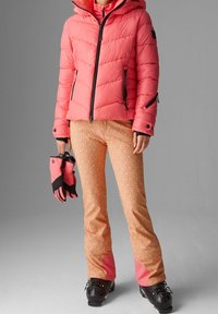 Rosa fluffig jacka med svarta accenter, mönstrade orange och rosa skidbyxor, svarta handskar och skidstövlar med detaljer.