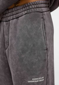 Grijze joggingbroek van een zachte katoenmix, met een elastische tailleband, zijzakken en witte geborduurde tekst op het onderbeen.