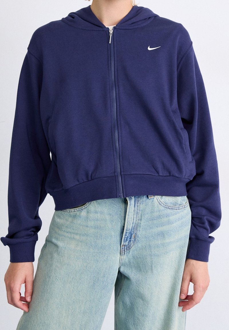 Marineblaues Zip-Up-Hoodie aus weichem Material, mit einem Frontreißverschluss, Kapuze mit Kordelzug und kleinem weißen Nike-Logo auf der linken Brust.