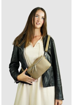 Beige strukturiere Umhängetasche mit einem Reißverschluss, dekorativen Quasten und einem verstellbaren Tragegurt, getragen über einer schwarzen Lederjacke.